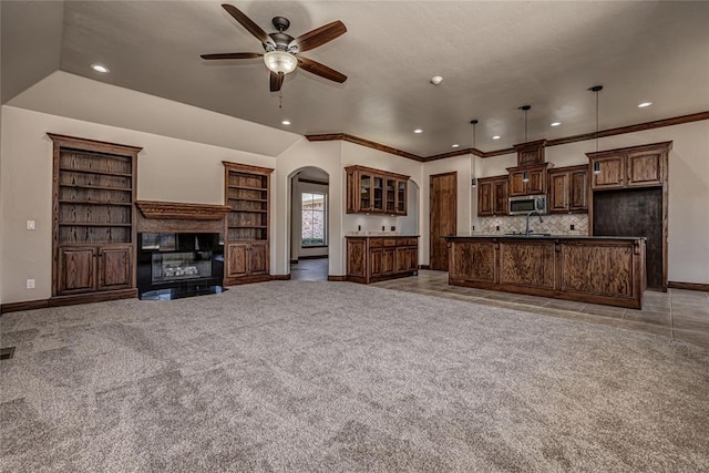 unfurnished living room with baseboards, ceiling fan, light colored carpet, arched walkways, and a glass covered fireplace