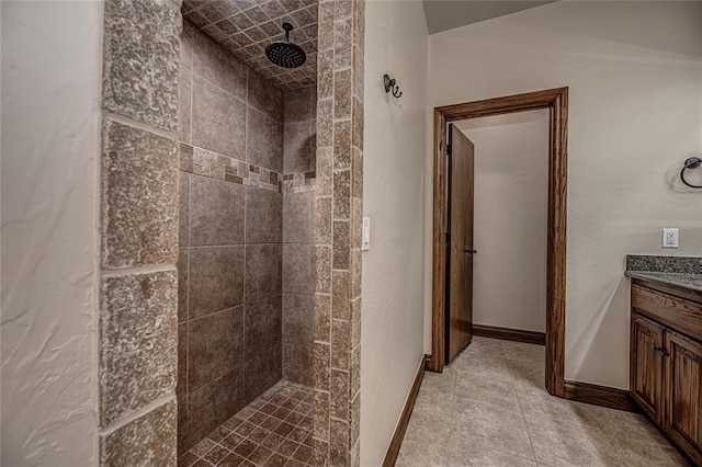 bathroom featuring baseboards, tiled shower, and vanity