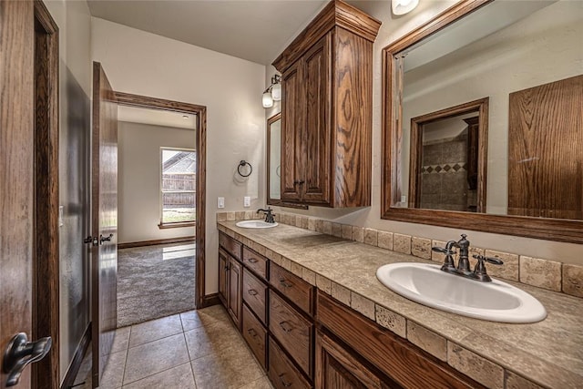 full bath with tile patterned floors, double vanity, baseboards, and a sink