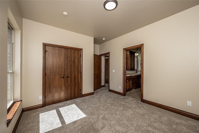 unfurnished bedroom featuring ensuite bath, carpet, a closet, and baseboards