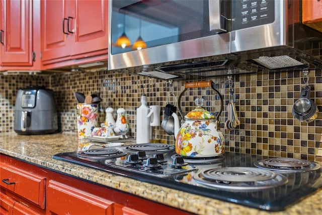 kitchen featuring stainless steel microwave, red cabinetry, black electric cooktop, and decorative backsplash