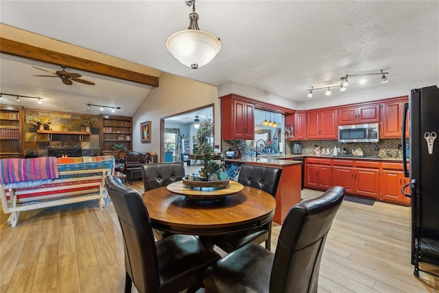 dining area featuring lofted ceiling with beams, a textured ceiling, a ceiling fan, and light wood finished floors