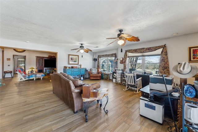 living area featuring light wood-style flooring, a textured ceiling, and a ceiling fan