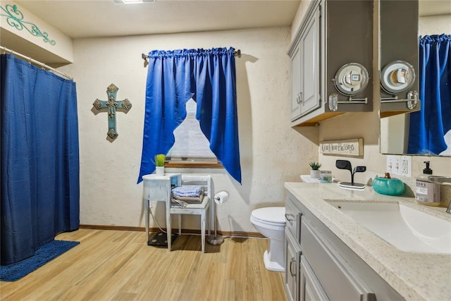 full bathroom with toilet, wood finished floors, vanity, and a textured wall