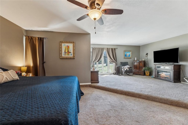 carpeted bedroom featuring a glass covered fireplace, baseboards, and ceiling fan