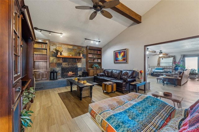 living room featuring built in features, wood finished floors, lofted ceiling with beams, a stone fireplace, and a textured ceiling