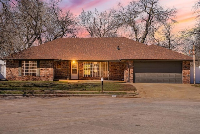 ranch-style house featuring a front lawn, driveway, a shingled roof, a garage, and brick siding