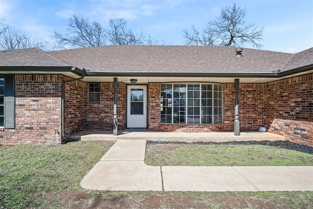 doorway to property with brick siding and a shingled roof