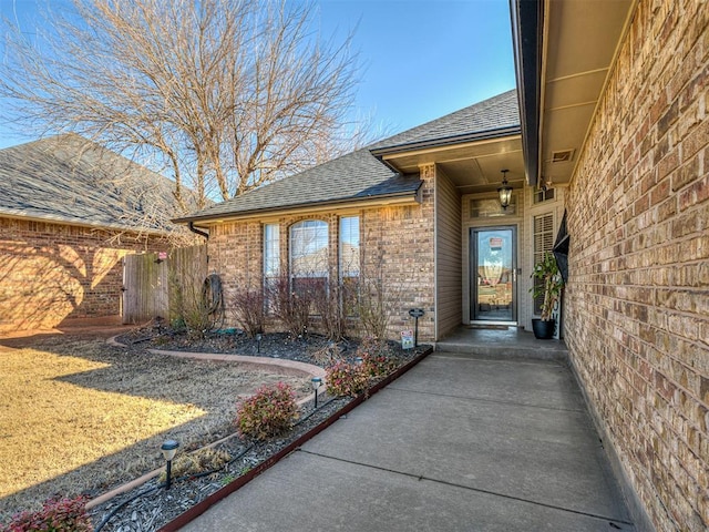 doorway to property with brick siding and roof with shingles