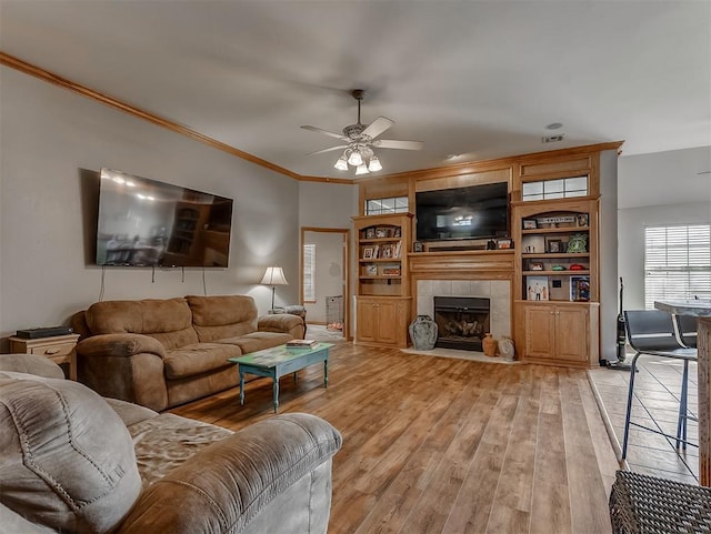 living room featuring visible vents, ornamental molding, a fireplace, light wood finished floors, and ceiling fan