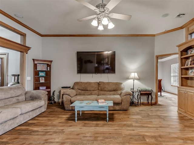 living room with crown molding, a ceiling fan, visible vents, and light wood finished floors