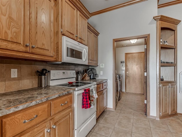 kitchen featuring dark countertops, washing machine and dryer, ornamental molding, light tile patterned flooring, and white appliances