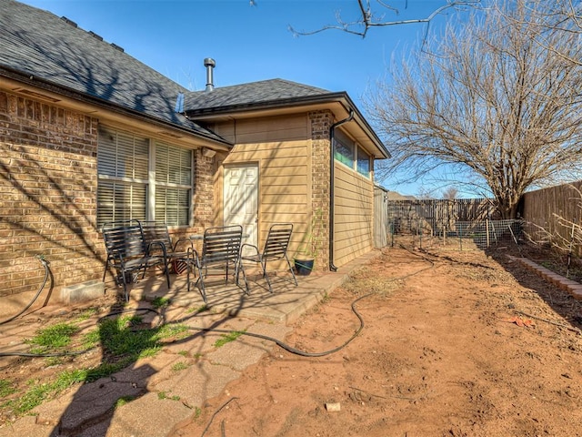 rear view of house with brick siding, a patio, a fenced backyard, and roof with shingles