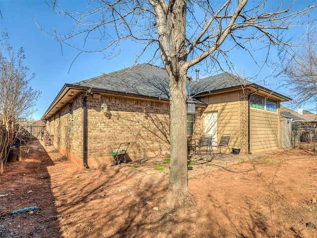 view of home's exterior featuring a patio area, brick siding, a shingled roof, and fence