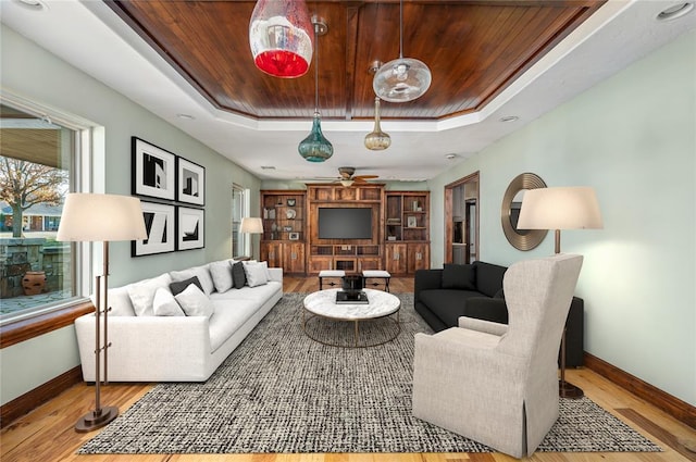 living room with a tray ceiling, wood finished floors, wood ceiling, and baseboards