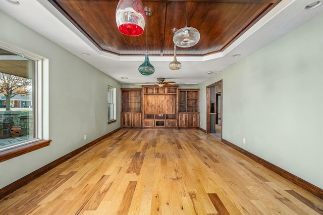 unfurnished living room with a tray ceiling, light wood finished floors, baseboards, and wooden ceiling