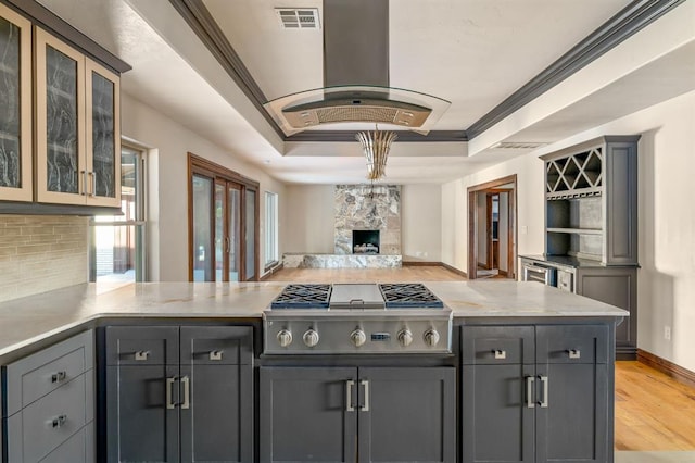 kitchen with stainless steel gas stovetop, visible vents, a tray ceiling, ornamental molding, and island range hood