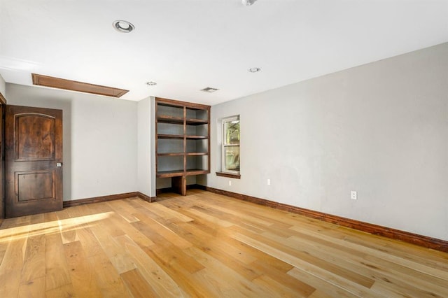 empty room with attic access, visible vents, light wood-type flooring, and baseboards