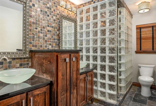 bathroom with toilet, stone tile floors, baseboards, walk in shower, and vanity