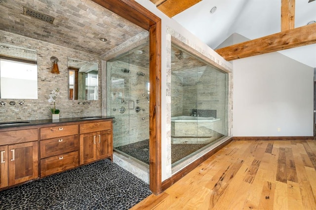 full bath with visible vents, a stall shower, wood finished floors, double vanity, and vaulted ceiling