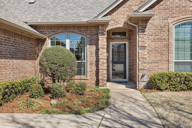 doorway to property with brick siding and a shingled roof