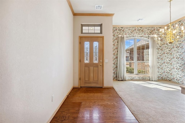 carpeted foyer featuring visible vents, baseboards, ornamental molding, wood finished floors, and a notable chandelier