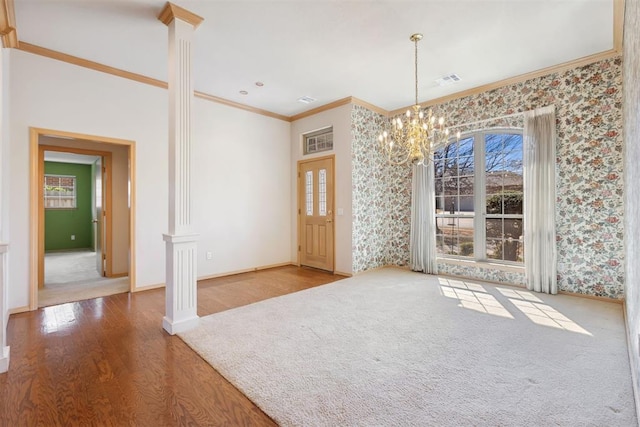 unfurnished dining area with a chandelier, ornamental molding, wallpapered walls, and decorative columns