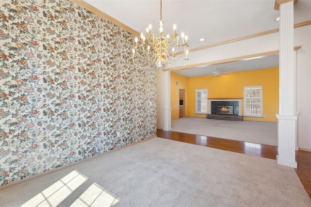 unfurnished living room with wallpapered walls, a brick fireplace, ornate columns, and ornamental molding