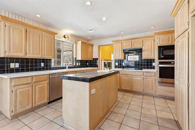 kitchen featuring visible vents, black appliances, light brown cabinets, under cabinet range hood, and a kitchen island