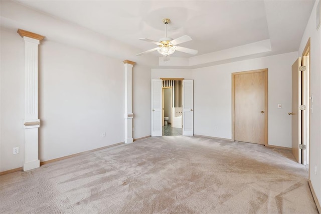 unfurnished bedroom featuring a tray ceiling, light colored carpet, ensuite bath, and ornate columns