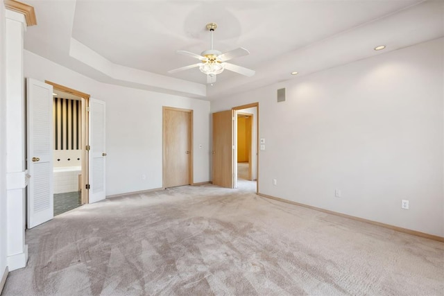 spare room with a tray ceiling, light carpet, baseboards, and a ceiling fan