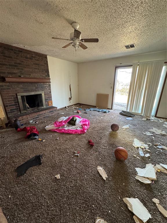 unfurnished living room featuring visible vents, a brick fireplace, a textured ceiling, and a ceiling fan