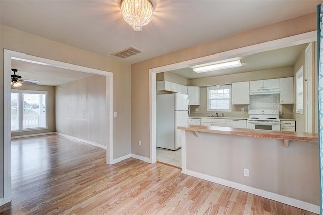 kitchen with white appliances, visible vents, a sink, light countertops, and under cabinet range hood