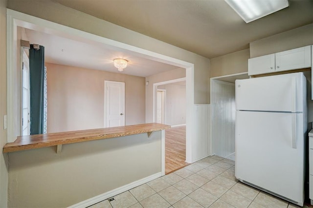 kitchen featuring a breakfast bar area, light tile patterned floors, a peninsula, freestanding refrigerator, and white cabinets