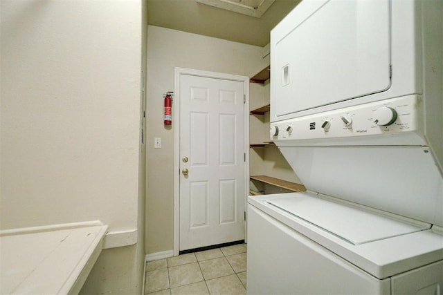 clothes washing area featuring laundry area, stacked washer and dryer, light tile patterned flooring, and baseboards