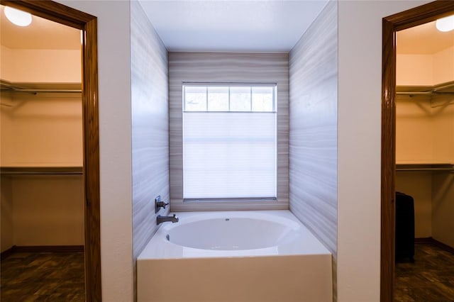 bathroom with a walk in closet, a garden tub, and baseboards