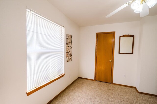 empty room featuring ceiling fan, light colored carpet, and baseboards