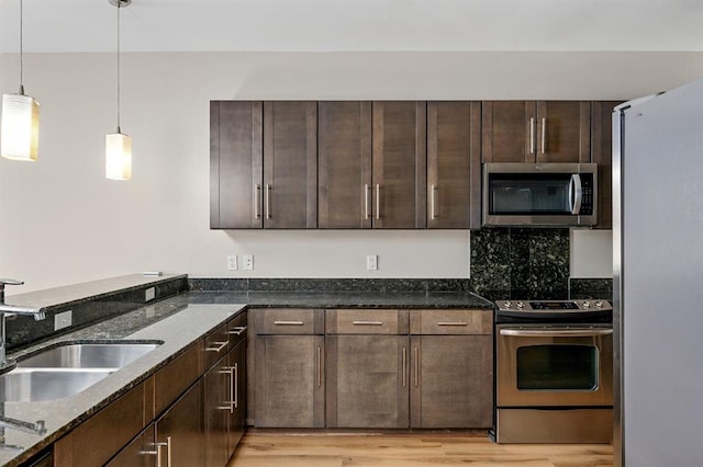 kitchen featuring a sink, dark stone counters, appliances with stainless steel finishes, light wood finished floors, and dark brown cabinets