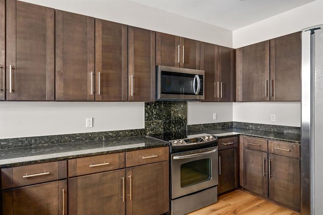 kitchen with light wood finished floors, dark brown cabinetry, dark stone countertops, and stainless steel appliances