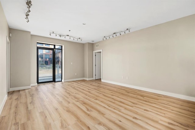 empty room with track lighting, visible vents, baseboards, and light wood finished floors