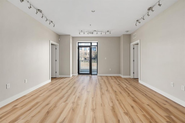 empty room featuring visible vents, baseboards, light wood-style flooring, and rail lighting