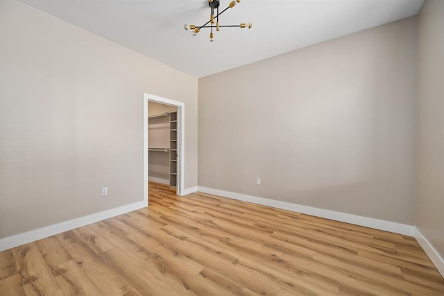 empty room with an inviting chandelier, baseboards, and light wood-style floors