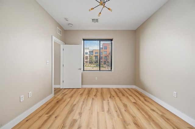 spare room featuring wood finished floors, baseboards, visible vents, and a chandelier