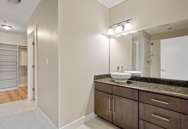 bathroom featuring marble finish floor, a tile shower, baseboards, a spacious closet, and vanity
