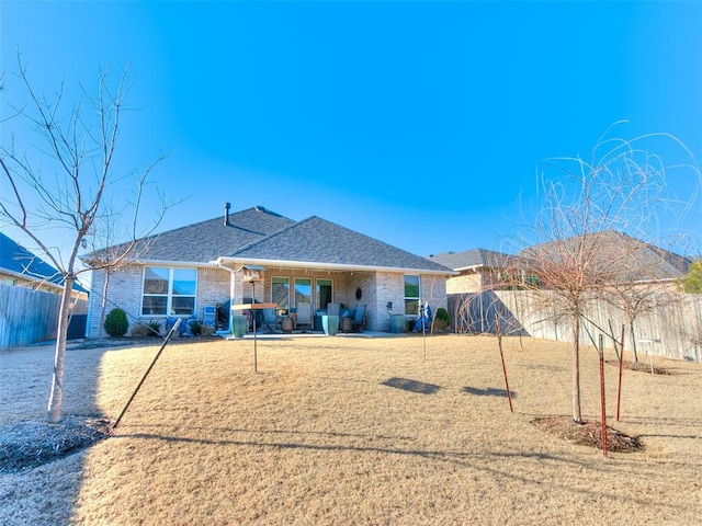 rear view of house with brick siding, roof with shingles, a lawn, a fenced backyard, and a patio area