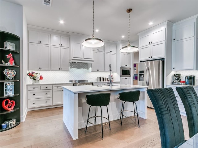 kitchen featuring a center island with sink, a sink, stainless steel appliances, light wood-style floors, and light countertops