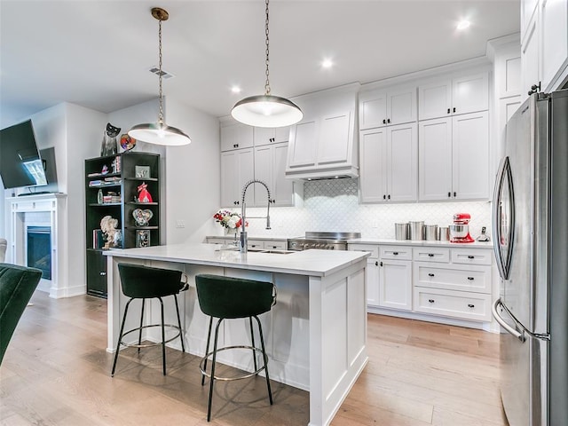 kitchen with a sink, light countertops, freestanding refrigerator, light wood-style floors, and a kitchen island with sink