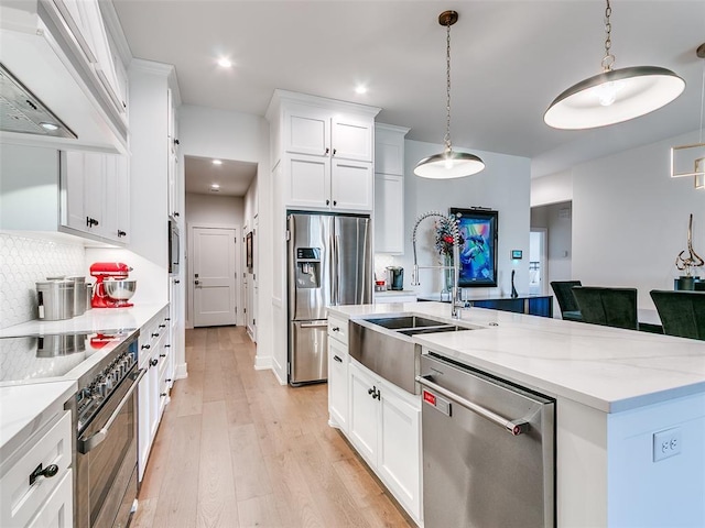 kitchen featuring a center island with sink, light wood finished floors, stainless steel appliances, white cabinets, and exhaust hood