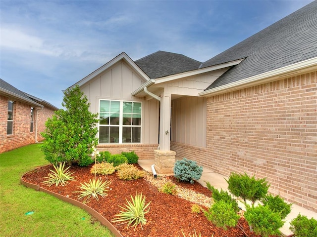 209 Pont Neuf Ct, Edmond, OK 73034 - view of exterior entry featuring board and batten siding, brick siding, a shingled roof, and a lawn