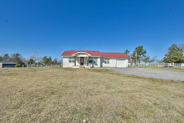 view of front of house with a front lawn, fence, gravel driveway, metal roof, and a garage